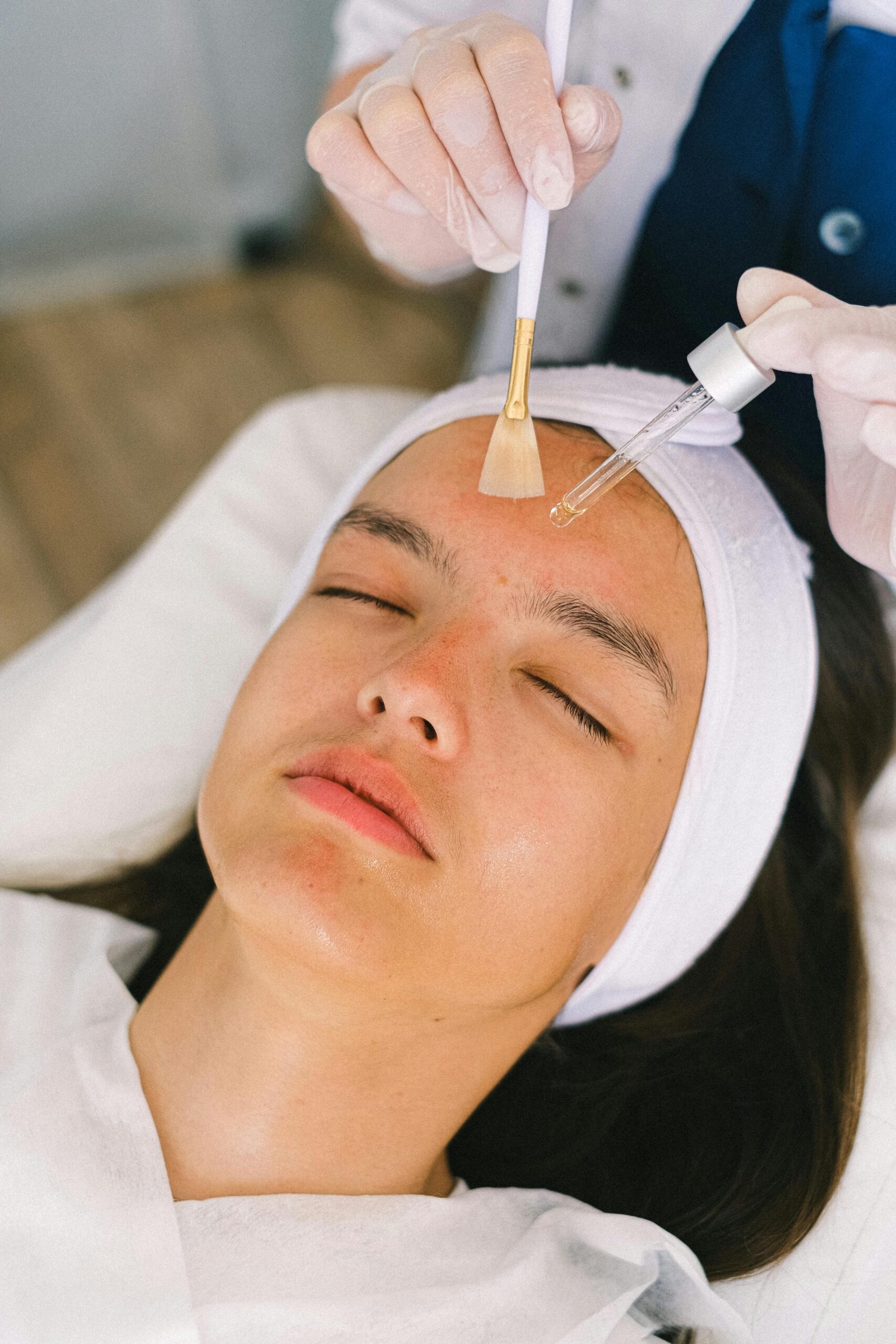 Woman receiving professional facial treatment with serum and brush at a modern spa.